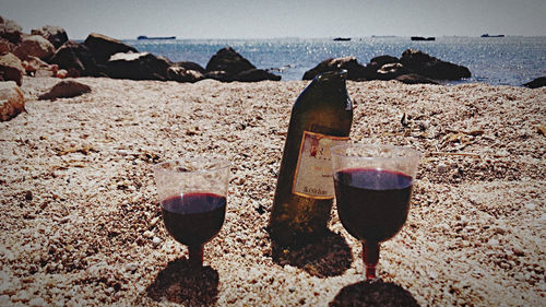 Close-up of wine glass on sand at beach against sky