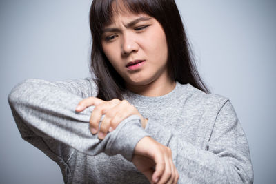 Young woman with arm pain against gray background