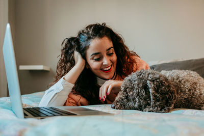 Smiling young woman with dog sitting on bed at home