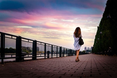 Rear view of woman standing on railing against sky