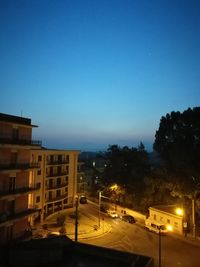 Illuminated city against clear blue sky at night