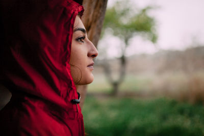 Close-up of young woman looking away standing by tree trunk