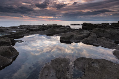 Rocks by sea against sky during sunset