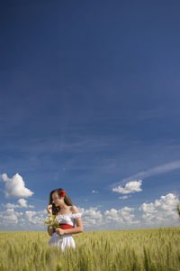 Woman smelling flower on field against sky