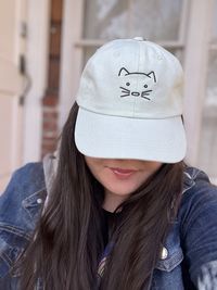 Portrait of young woman in a jean jacket wearing hat with a cat face embroidered on it