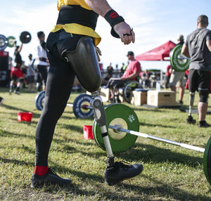 Low section of male adaptive athlete standing by deadlift on grassy field at park