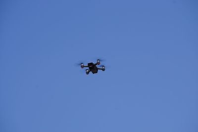 Low angle view of quadcopter flying against clear blue sky during sunny day