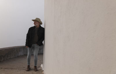 Portrait of adult man in cowboy hat and jeans against wall.