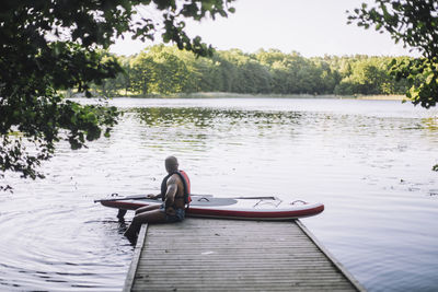 Man with paddleboard looking at lake while sitting on jetty