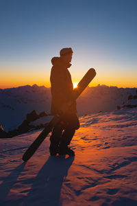 Skier stands on top of a snowy hill at a ski resort during a calm winter sunset. athlete scenery