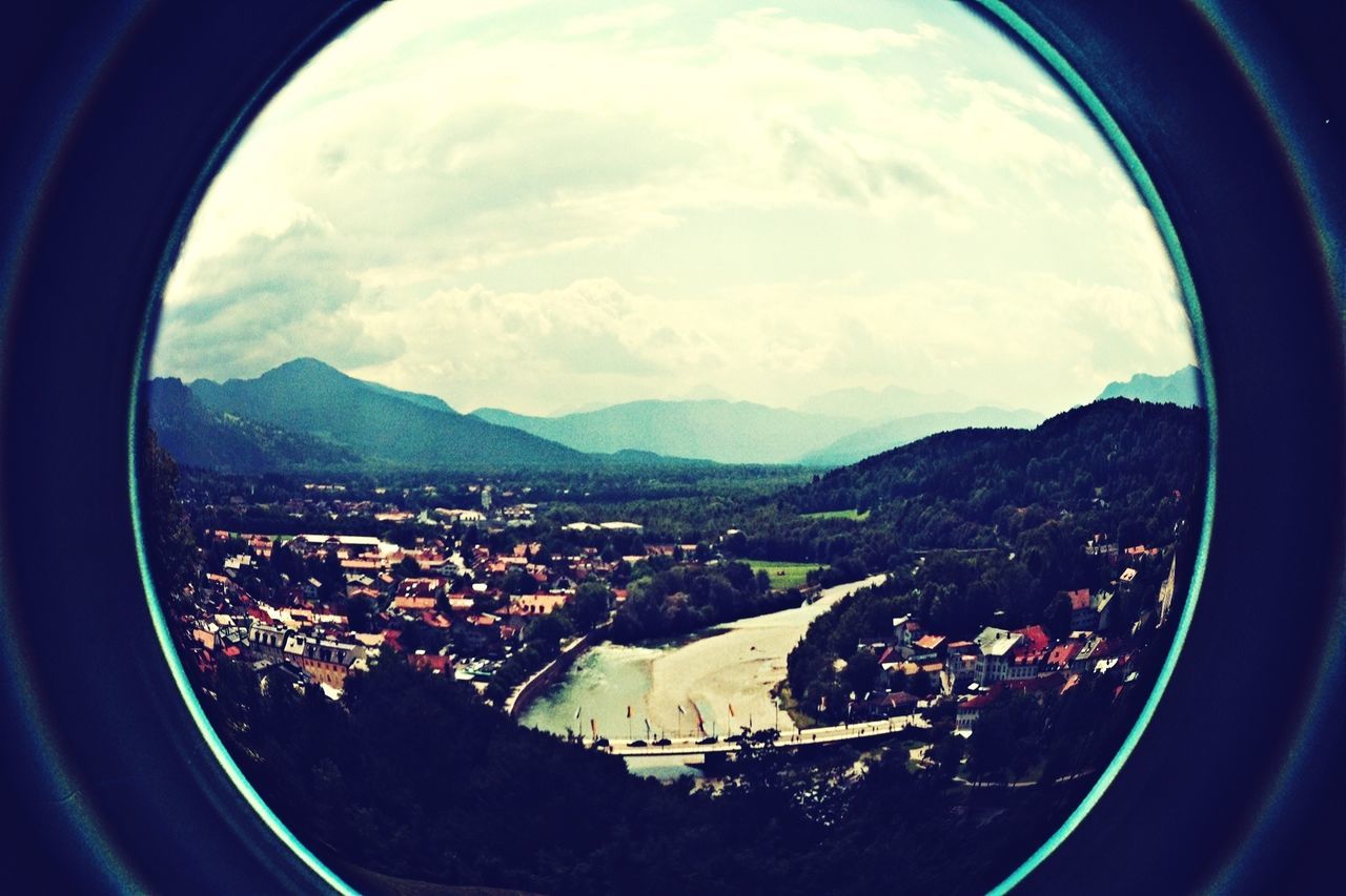 sky, window, indoors, landscape, cloud - sky, fish-eye lens, transparent, aerial view, transportation, cityscape, mountain, glass - material, built structure, cloud, architecture, no people, high angle view, vehicle interior, city, nature