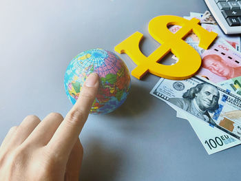 Close-up of hand over globe by dollar sign with paper currency and calculator