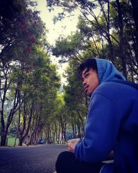 Side view of young man looking away against trees