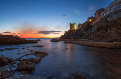 Scenic view of sea by buildings against sky during sunset