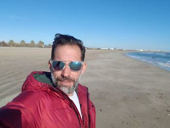 Portrait of mature man wearing sunglasses at beach against clear sky