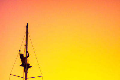 Silhouette person standing on sailboat against orange sky
