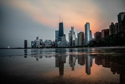 Reflection of buildings at beach against sky in city