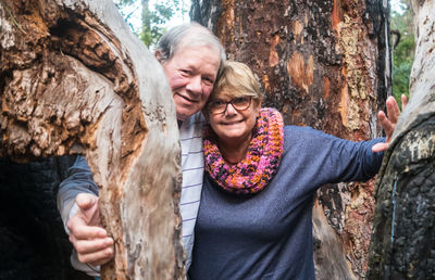 Portrait of smiling senior couple standing against tree trunk