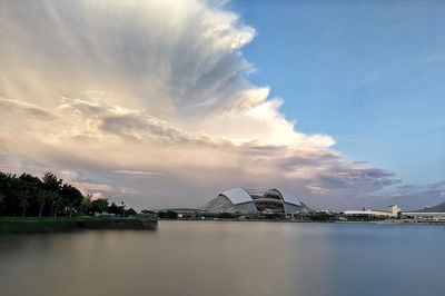 View of city at waterfront against cloudy sky