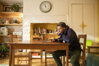 Freelancer eating meal using laptop at desk in home