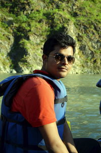 Portrait of man in sunglasses sitting at lake during sunny day