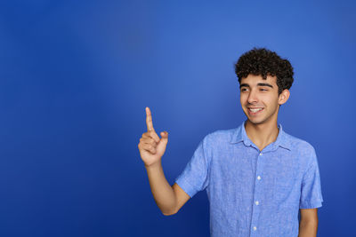 Portrait of young woman with arms raised against blue background