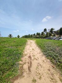 Dirt road amidst field against sky