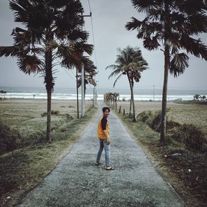 Man standing by palm trees on shore against sky