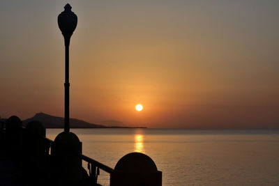 Silhouette street light by sea against sky during sunset