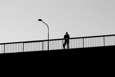 Rear view of silhouette man standing on bridge against clear sky
