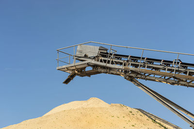 Conveyor belt over heaps of gravel against the blue sky at an industrial cement plant.