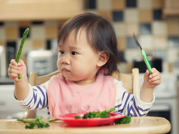 Baby girl with vegetables sitting on high chair at home