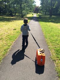 Rear view of boy walking on street with luggage