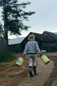 A girl in casual clothes walks along the road holding cans in her hands