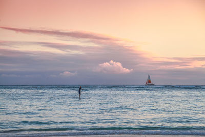 Man paddleboarding on sea against sky during sunset