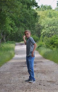 Full length of boy standing on road amidst trees