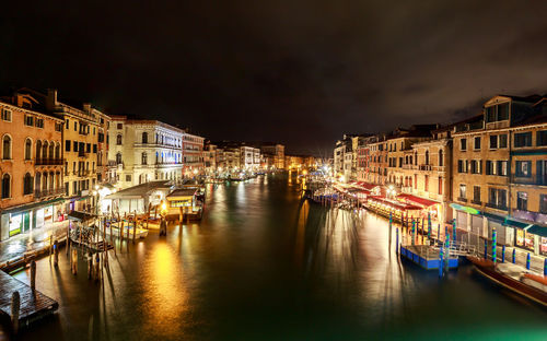 Boats moored in canal amidst buildings in city at night