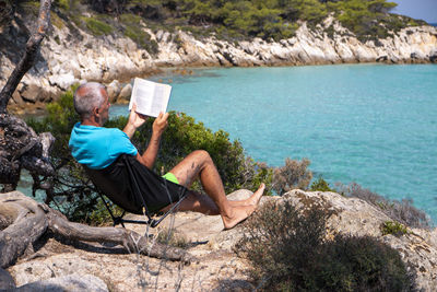 Man lying on a deckchair and reading a book. happy mature man next to the beach with beautiful view