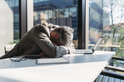 Tired businessman sitting at desk by window in office