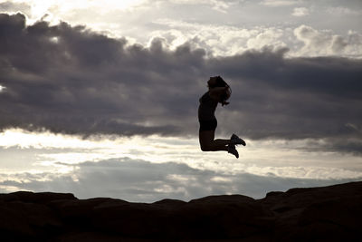 Low angle view of man jumping against cloudy sky