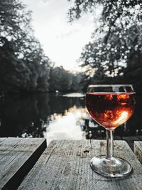 Red wine on table by lake against trees