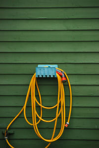 Garden hose hanging on green wall at yard