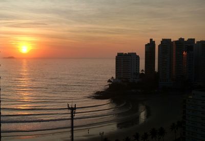 Silhouette buildings by sea against sky during sunset