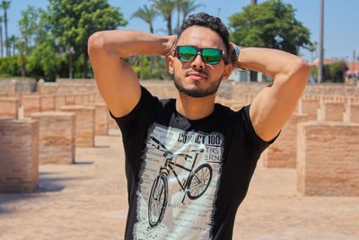 Young man wearing sunglasses standing against wall