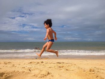 Side view of shirtless boy jumping on sandy beach