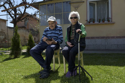 Full length of senior couple sitting at backyard against house