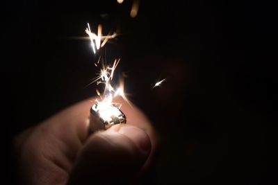 Close-up of hand holding lit candle in the dark