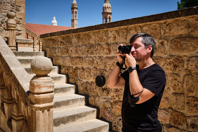 Portrait of young adult male tourist taking a photo of famous site. stone stairway at background