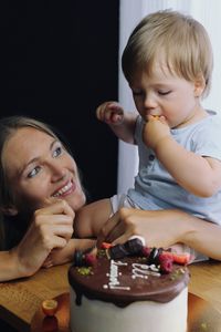 Portrait of blonde cute boy with mother eating cake at his birthday