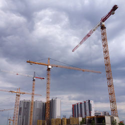 Low angle view of cranes at construction site against sky